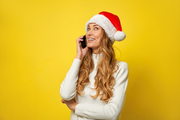 Gelbe Wand der Weihnachtsmann-Weihnachtsmütze der Frau mit Smartphone in der Hand