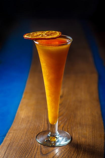 Gelber alkoholischer Perlmuttcocktail in einem langen Glas mit getrockneter Orange oben auf einem Holztisch. Helles buntes Getränk. Speicherplatz kopieren