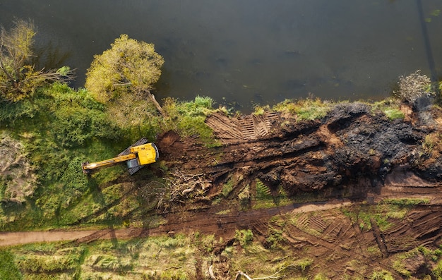 Gelber Bulldozer, der einen Fluss gräbt, um einen Flusskanal zu vertiefen und zu säubern, um den Wasserfluss zu verbessern.