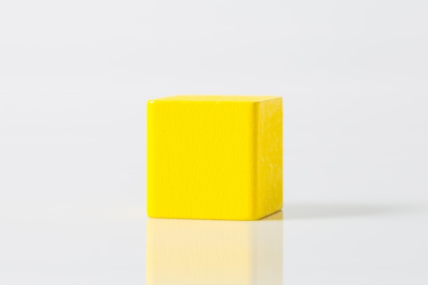 Gelber geometrischer hölzerner Formwürfel lokalisiert auf Weiß