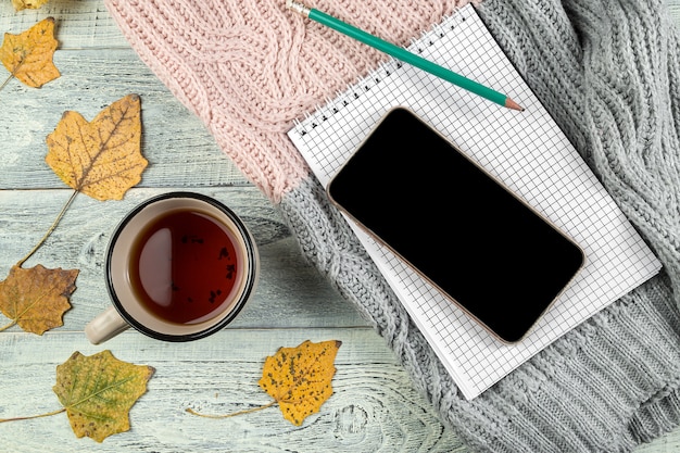 Gelber Herbstlaub, eine Tasse Tee und ein Smartphone auf einem alten hölzernen Hintergrund