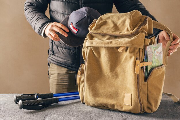 Gelber Hipster-Rucksack mit Karte und Trekking-Wanderstock. Männlicher Reisender, der sich auf eine Wanderung in den Bergen vorbereitet