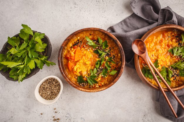 Gelber indischer veganer Linsensuppecurry mit Petersilie und indischem Sesam in einer hölzernen Schüssel.