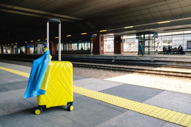 Gelber Koffer mit ukrainischer Flagge am Bahnhof