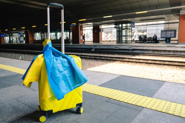 Gelber Koffer mit ukrainischer Flagge am Bahnhof