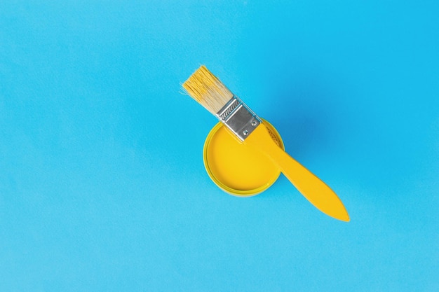 Gelber Pinsel mit einer Dose gelber Farbe auf blauem Hintergrund Trendfarben Minimales Konzept der Innenauswahl Flache Lage