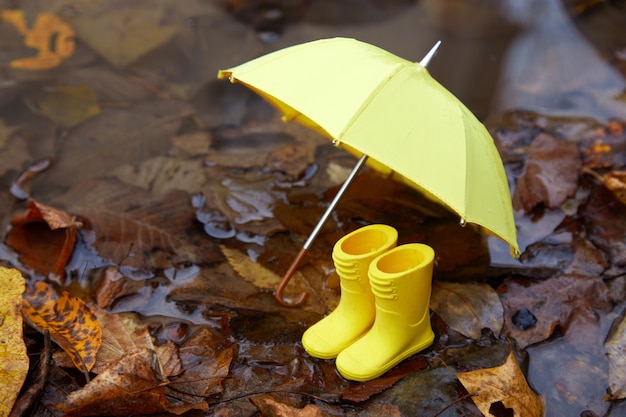 Foto gelber regenschirm und gummistiefel in einem poddle mit herbstherbstblättern