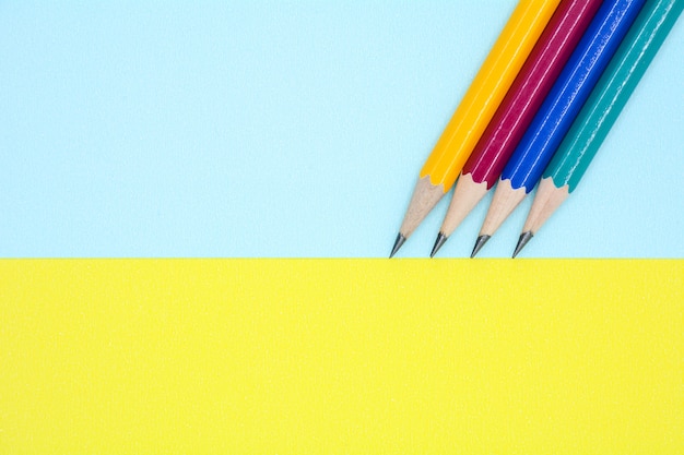 Gelber, roter, blauer und grüner Bleistift auf blauem und gelbem Papier - Hintergrund