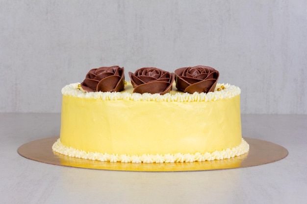 Gelber Sahnekuchen mit braunen Rosen auf einer grauen Hintergrundnahaufnahme