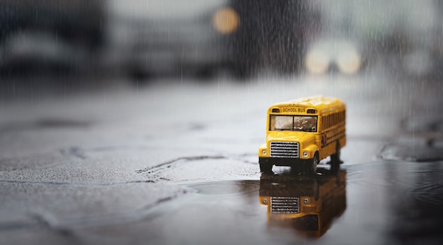 Gelber Schulbus (Spielzeugmodell) während des harten Regenfalls in der Stadt, Ansicht des niedrigen Winkels und der geringen Schärfentiefe Zusammensetzung.
