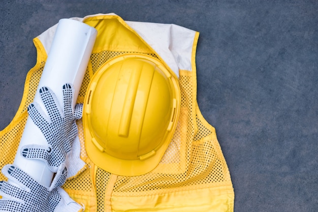 Gelber Schutzhelm mit Handschuh, Blaupause auf Weste auf Betonboden