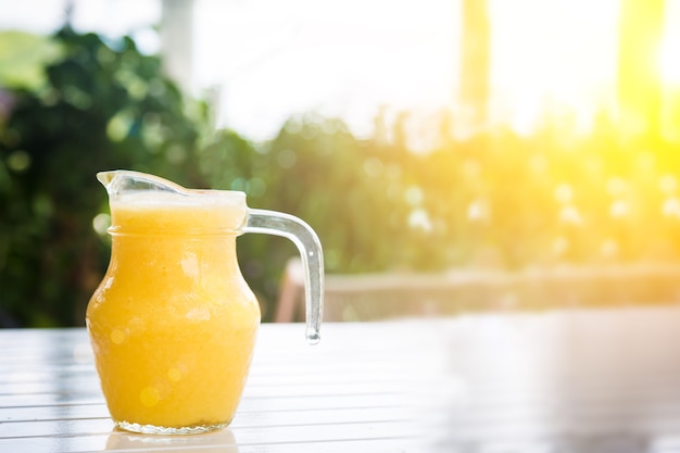 Gelber Smoothie aus tropischen Früchten auf dem weißen Holztisch im Krug am sonnigen Tag