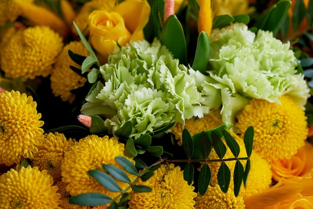 Gelber Strauß mit grüner Nelke in der Komposition von Chrysanthemen, Rosen und gefärbten Körnern