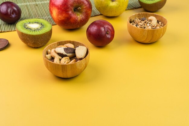 Gelber Tisch mit frischen Früchten wie Apfel-Kiwi-Pflaume-Birne-Kastanien und Müsli