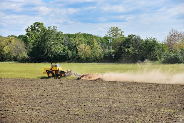 Foto gelber traktor bereitet land für die aussaat vor anbaufeld und blauer himmel landwirtschaft und maschinenkonzept