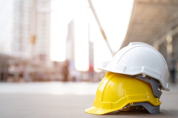 Gelber, weißer harter Sicherheitshelmhut im Projekt am Baustellengebäude auf Betonboden auf Stadt. Helm für Arbeiter als Ingenieur oder Arbeiter