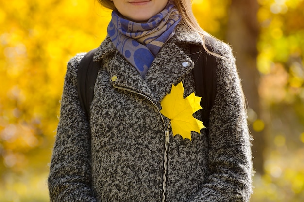 Gelbes Ahornblatt auf einem grauen Mantel. Herbst-Konzept.