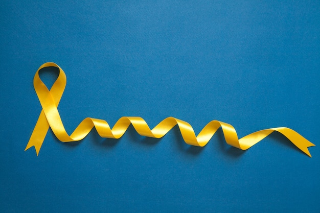 Gelbes Band auf dem blauen Grübchenhintergrund. Konzept zur Sensibilisierung für Krebs bei Kindern. Krebskonzept.