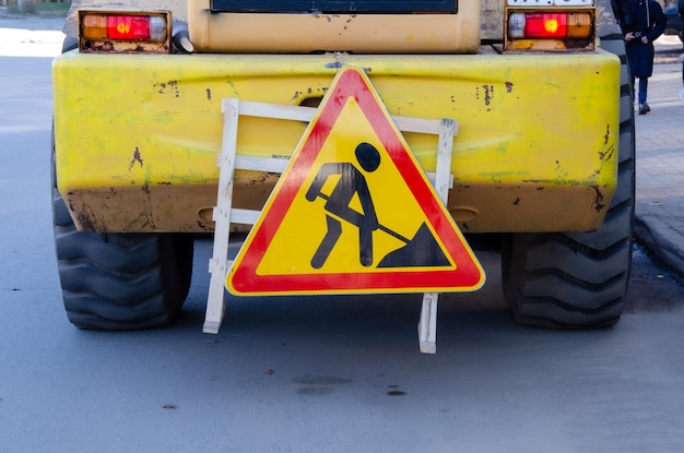 Gelbes dreieckiges Warnschild in Arbeit neben Baumaschinensicherheit von Straßenarbeiten