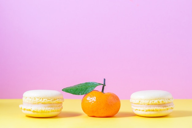 Gelbes französisches Makronengebäck mit Zitronencreme auf Gelb und Rosa mit orangefarbener Mandarine