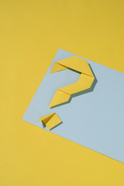 Gelbes gefaltetes Papier-Origami-Fragezeichen auf einem blauen Banner über einem passenden gelben Hintergrund mit Kopienraum zur Verwendung als Designvorlage