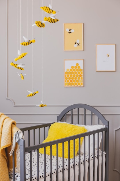 Gelbes Kissen in einem Krippenbienenposter und hängende Dekoration in einem Kleinkinderzimmer Echtes Foto