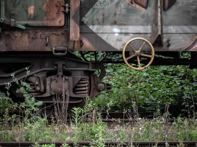 Gelbes Metallrad, das für die Feststellbremse des Fahrzeugs verwendet wird, das sich an der Seite eines Waggons befindet, der auf einer Bahnstrecke voller Vegetation geparkt ist