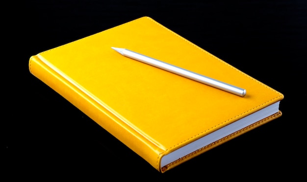 Gelbes Notizbuch mit Stift auf schwarzem Hintergrund