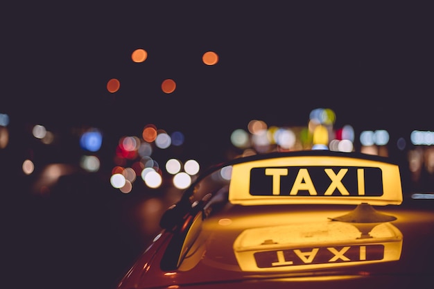Gelbes und schwarzes Schild eines Taxis, das nachts an einem Auto angebracht ist