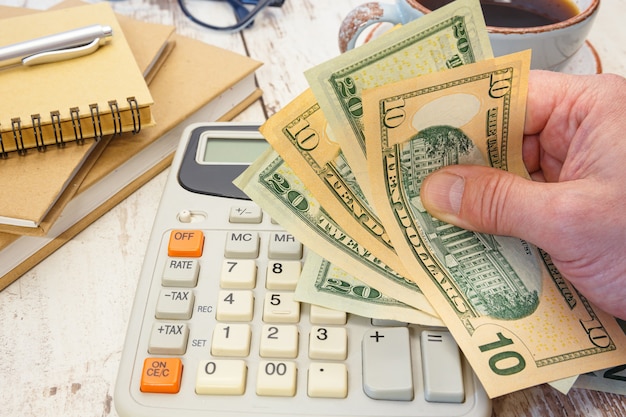 Foto geld in der hand neben einem taschenrechner und bürobedarf. finanzielles konzept.