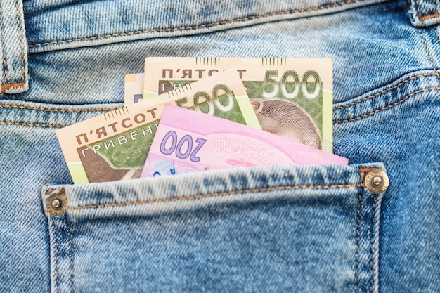 Geld in der hinteren Blue Jeans-Tasche. Denim-Textur-Hintergrund. Ukrainische fünf- und zweihundert Griwna. Nationale Banknoten. Finanz-, Wirtschafts- und Modekonzept.