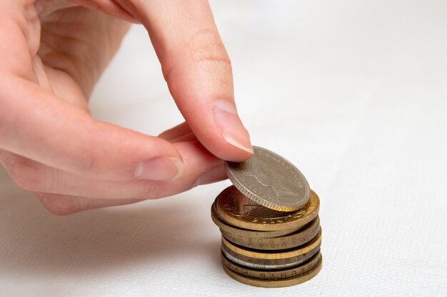 Geld sparen, legt eine Hand Münzen verschiedener Länder in einen Stapel, weißer Hintergrund, Nahaufnahme.