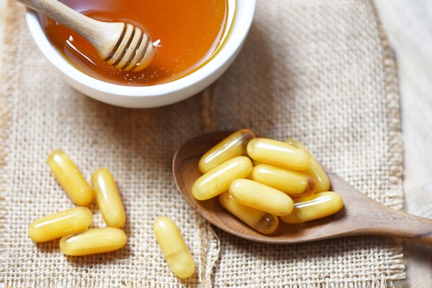 Gelée Royale-Kapseln im Holzlöffel auf Sack und Honig in der Schale - gelbe Kapselmedizin oder Ergänzungslebensmittel von der Natur für Gesundheit
