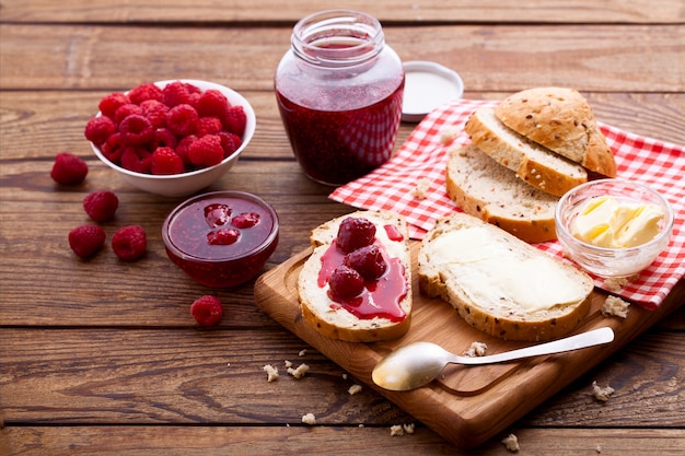 Geléia de framboesa, pão e manteiga com frutas vermelhas na mesa de madeira