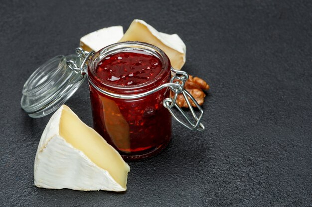 Geléia de framboesas e pedaços de queijo brie no backround concreto escuro