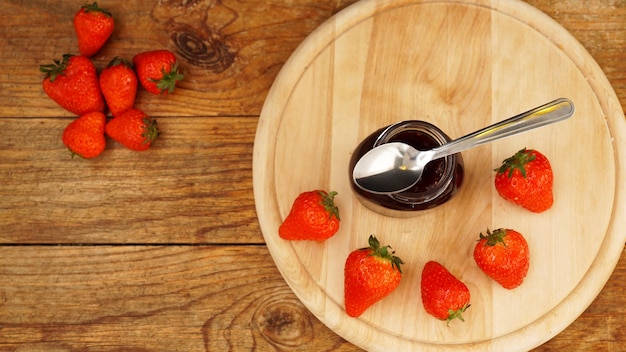 Geléia de morango na jarra de vidro com frutas frescas em fundo de madeira