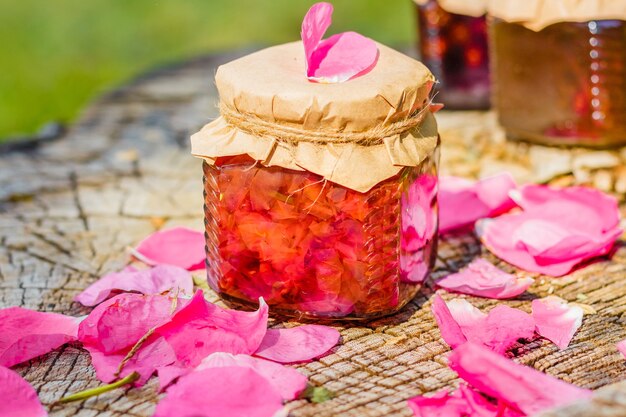 Geléia de rosa com pétalas de rosa em um toco de madeira. Natureza morta ao ar livre