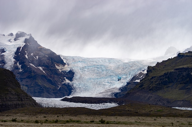 Geleira com cinzas no gelo com água derretida e paisagem islandesa