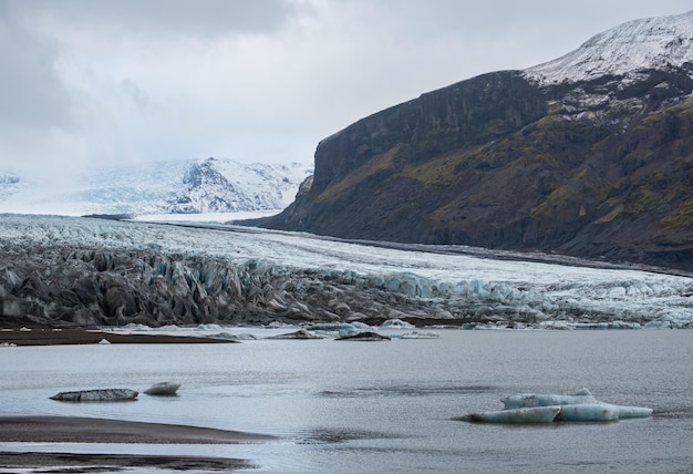 Geleira Skaftafellsjokull A língua da geleira da Islândia desliza da calota de gelo Vatnajokull ou da geleira Vatna perto do vulcão subglacial Esjufjoll Lagoa glacial com blocos de gelo e montanhas circundantes