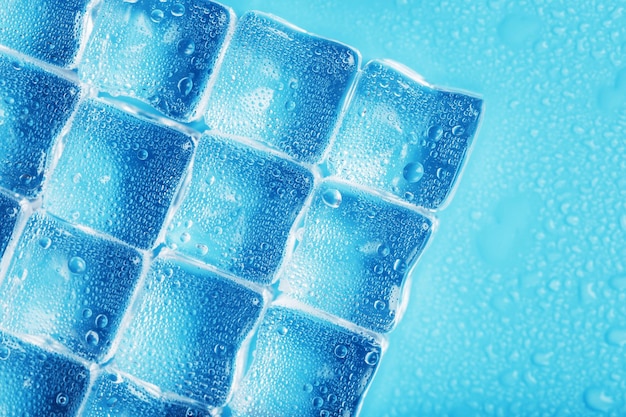 Gelo feito de cubos alinhados com gotas em um fundo azul