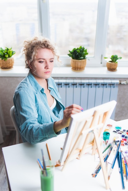 Gelockte blonde Frau, die ein Bild durch das Fenster malt