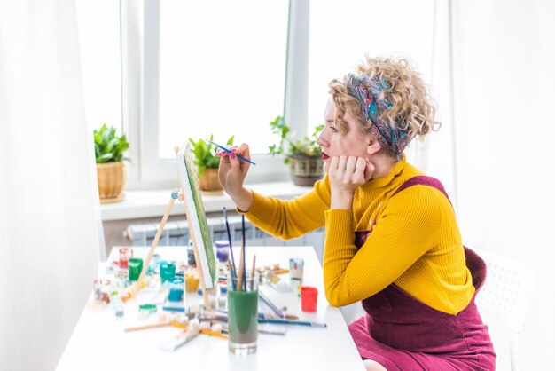 Gelockte blonde Frau, die ein Bild durch das Fenster malt