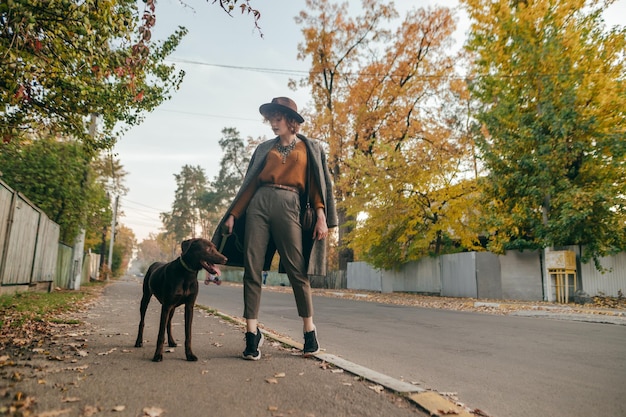 Gelockte Dame mit Hut geht mit einem Hund auf der Dorfstraße spazieren