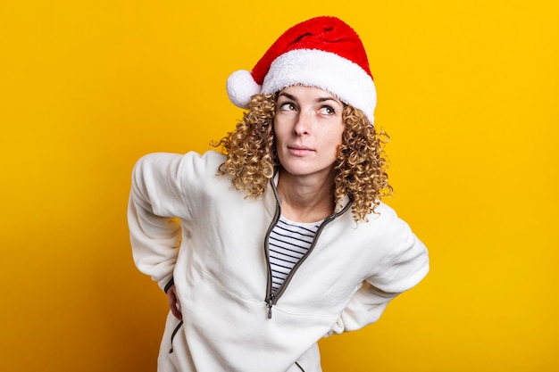 Gelockte junge Frau in Weihnachtsmann-Hut auf gelbem Grund.