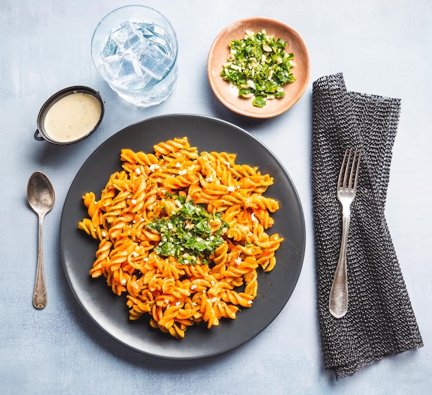 Gelockte Nudelmakkaroni mit Tomaten- und Gremolata-Sauce in einem runden dunklen Teller auf einem Tisch