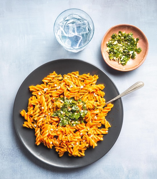 Gelockte Nudelmakkaroni mit Tomaten- und Gremolata-Sauce in einem runden dunklen Teller auf einem Tisch