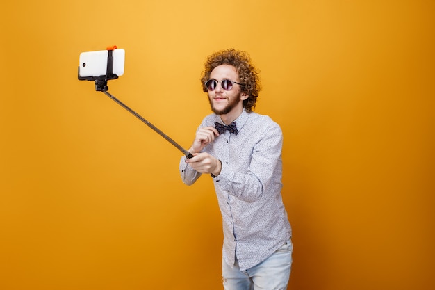 Gelockter Mann in der Sonnenbrille und in Fliege, die selfie unter Verwendung m nehmen