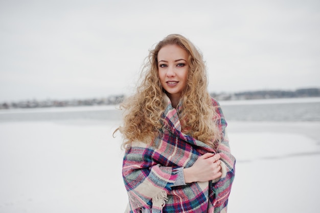 Gelocktes blondes Mädchen im karierten Plaid gegen zugefrorenen See am Wintertag