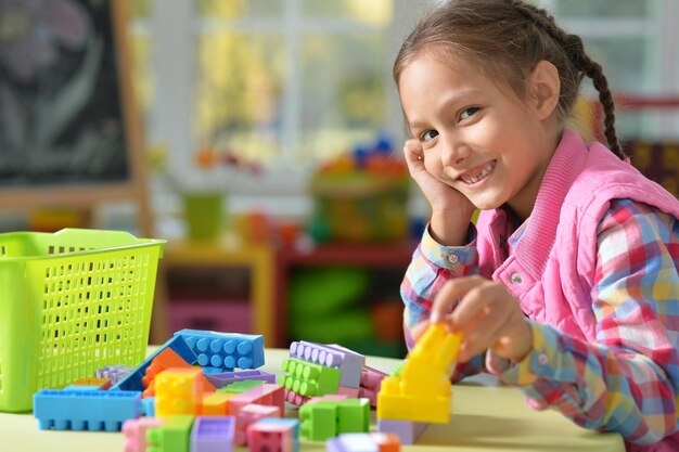 Gelocktes kleines Mädchen, das mit bunten Plastikblöcken spielt