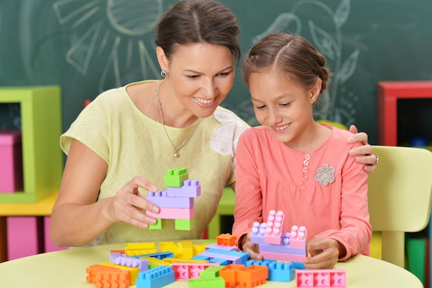 Gelocktes kleines Mädchen und ihre Mutter, die mit buntem Plastik spielen b